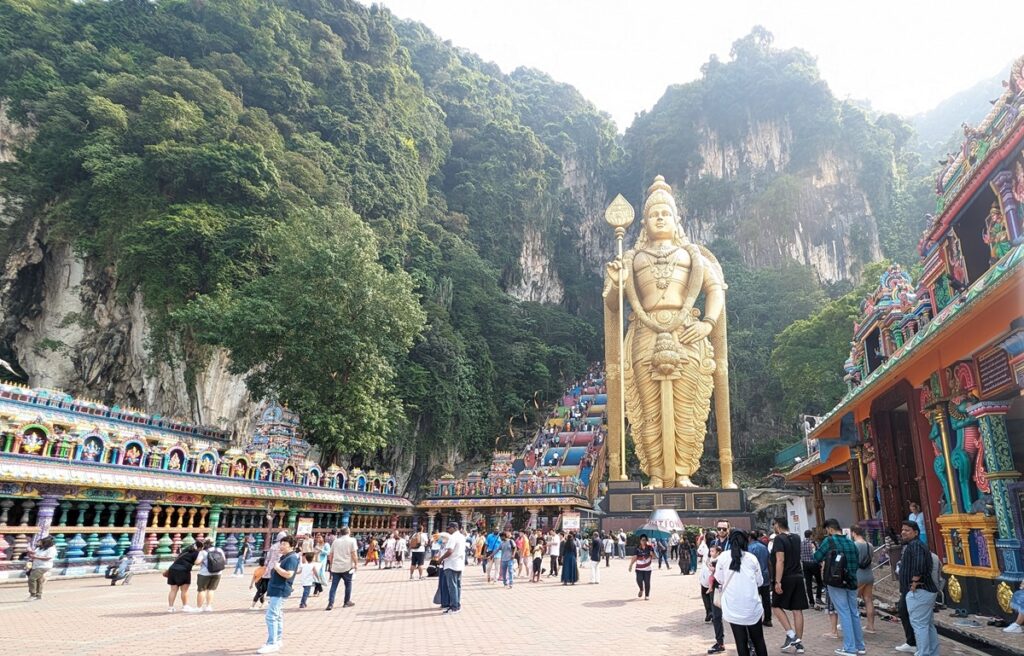 クアラルンプール近郊のバトゥ洞窟入口に立つ黄金のムルガン神像と石灰岩の山