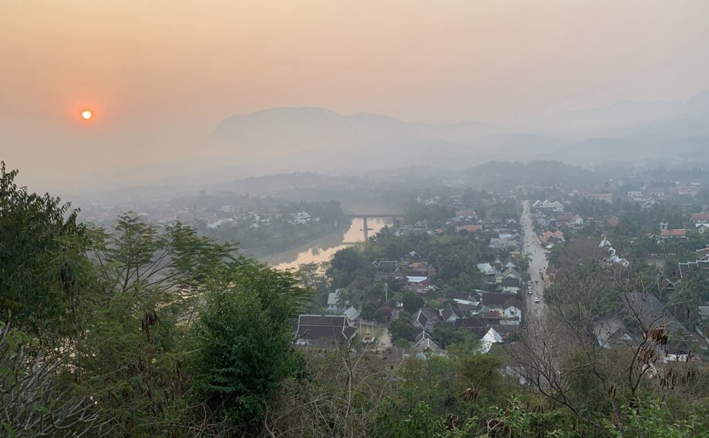 高台からルアンパバーンの街並みと山々、川、低い位置にある太陽を眺めた景色