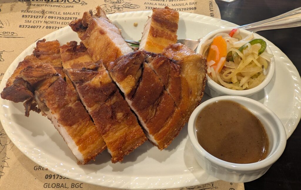 カリカリに揚げた皮付き豚肉レチョン・カワリに付け合わせとソースが添えられた料理