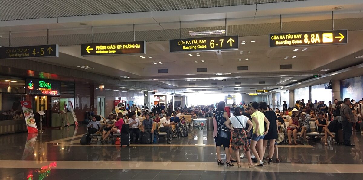 ハノイの空港内にある搭乗ゲート前の待合エリア。頭上には搭乗ゲート4〜8Aの案内表示があり、多くの乗客が椅子に座って出発を待っています。