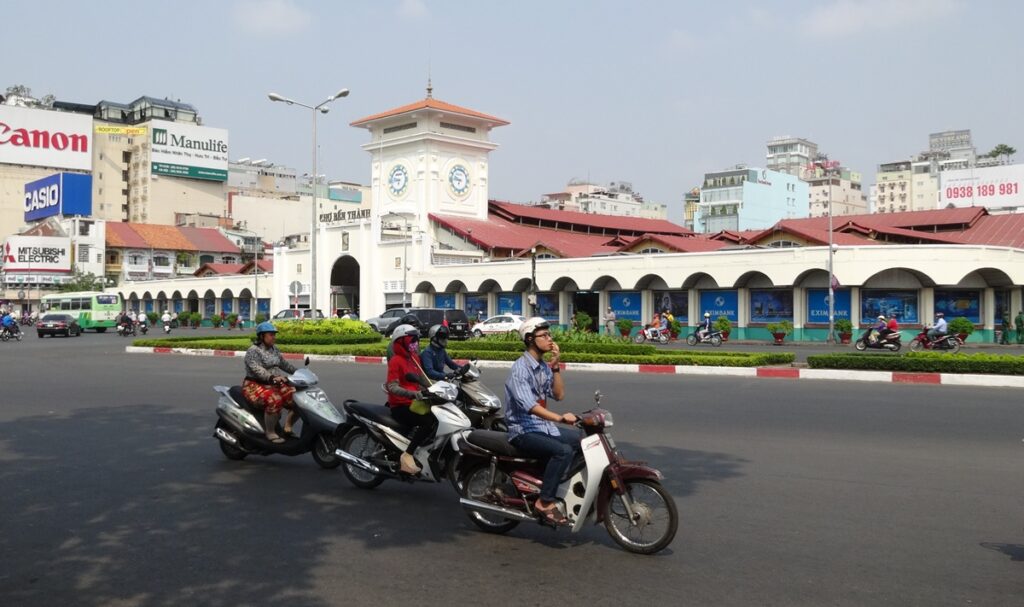 ホーチミンのベンタイン市場前を多数のバイクが行き交う様子と時計塔のある市場外観