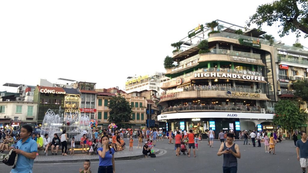 ハノイ旧市街のドンキンギアトゥック広場周辺に観光客や地元の人が集まり、カフェや商業施設が並ぶ様子