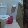 洋式便器の横には手動式の洗浄シャワーが設置されており、ピンク色のゴミ箱やトイレットペーパーが確認できる。