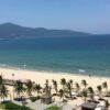 高台から見る、青く広がる海と白い砂浜、ヤシの木が並ぶリゾートエリア。遠くには山並みが見え、開放感のある景色が広がっている。