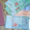 木目のテーブルの上に、日本のパスポートとマレーシアの通貨1・5・10・50リンギット紙幣が並べられているが並べられています。1・5・10・50リンギット札が確認でき、