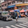 フィリピン名物のジープニーや小型車が行き交い、カラフルなパラソルの下に露店が並んでいる。歩行者も多く、マニラの庶民的で活気のある街並み。