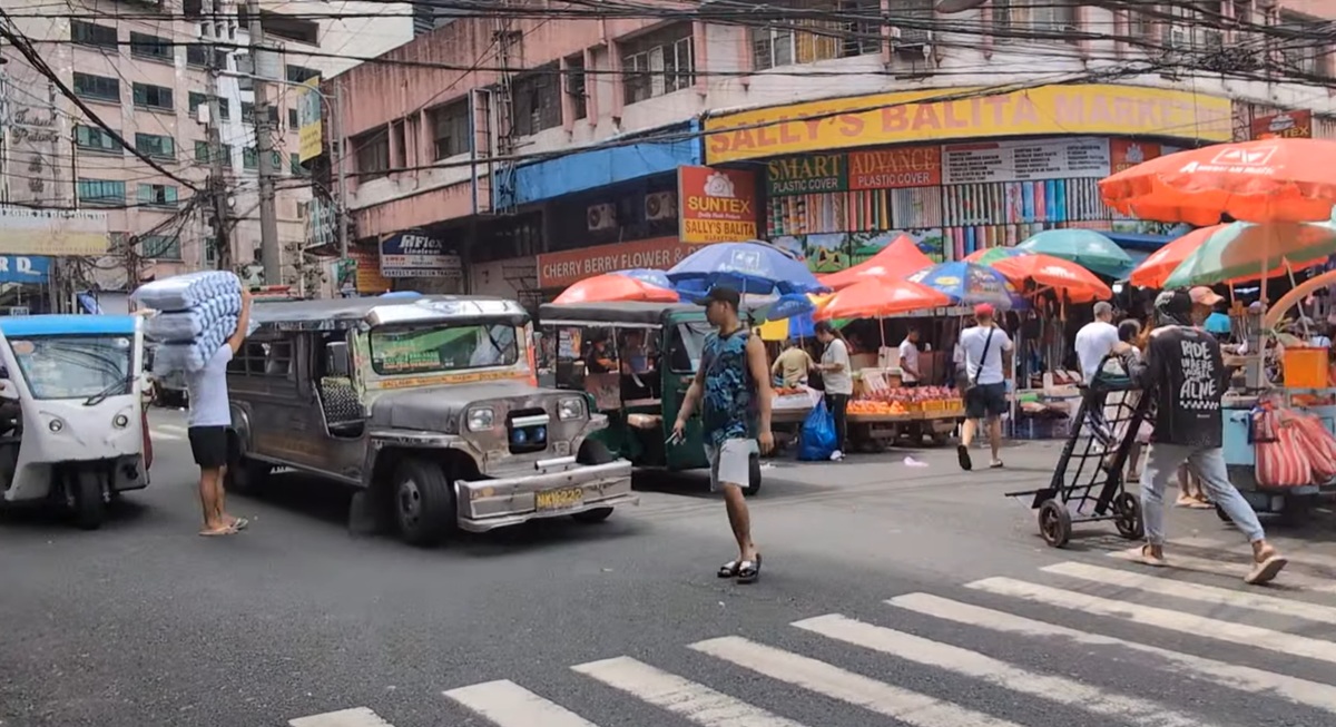 フィリピン名物のジープニーや小型車が行き交い、カラフルなパラソルの下に露店が並んでいる。歩行者も多く、マニラの庶民的で活気のある街並み。